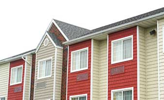 Exterior of a building with alternating beige and red siding, white-framed windows, and a gabled roof featuring brick accents.