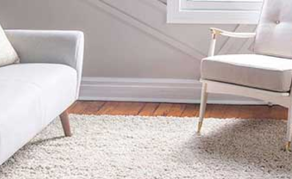 A white sofa and matching armchair with wooden accents sit on a white shag rug in a living room.