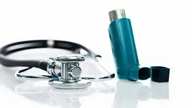 Stethoscope and uncapped blue asthma inhaler on a white surface.