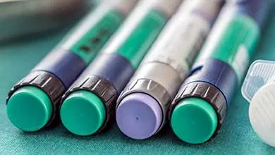 Insulin pens with green and purple caps, lined diagonally on a green surface.
