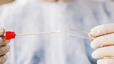 Gloved hand holding a red-capped testing swab and clear vial.