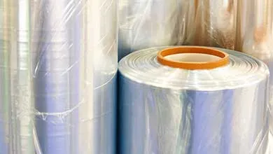 Close-up of several large, clear industrial plastic film rolls; one roll lies on its side, revealing a cardboard core.