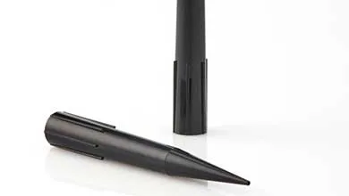 Two identical black plastic ground stakes. One lies on a white surface, pointed tip visible. The other stands upright in the background.