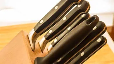 Close-up, angled view of several black-handled knives stored in a light wood knife block.