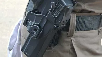 Close-up of a black handgun in a holster on the hip of a person wearing khaki pants and a black belt.