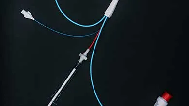 Close-up of medical equipment on a black surface: bright blue and red tubing attached to a syringe and several white plastic ports.