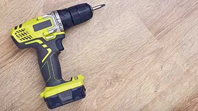 A yellow-green and black cordless drill on a light wood surface.