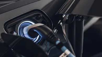 Electric vehicle charging cable plugged into a car, with illuminated charging port detail.