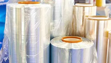 Close-up of several large rolls of clear plastic wrap with shiny surfaces, each wound around an orange cardboard core.