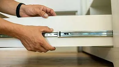 Hands installing a white drawer onto metal slide tracks.