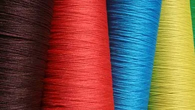 Close-up of large spools of thread in dark brown, red, blue, and yellow, arranged vertically.