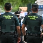 Two Guardia Civil officers, seen from behind, wear dark green uniforms with "GUARDIA CIVIL" in yellow on their backs.