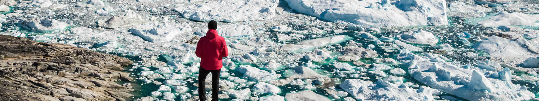 Travel in arctic landscape nature with icebergs - Greenland tourist man explorer - tourist person looking at amazing view of Greenland icefjord - aerial drone image. Man by ice and iceberg, Ilulissat.